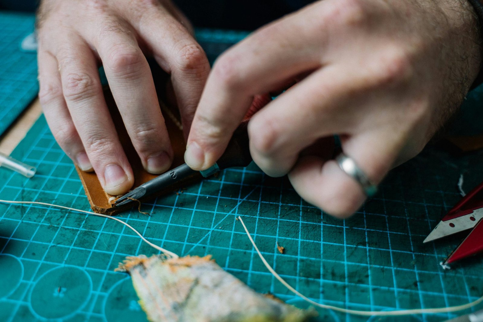 Artisan meticulously crafting leather with precision tools on a workshop table.